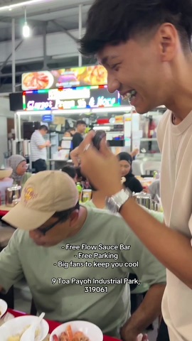 Two customers eating at the stall counter, with the free flow sauce bar and free parking listed on screen